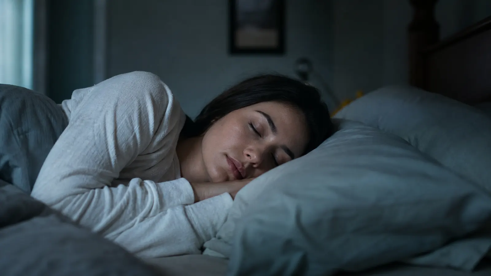 Woman sleeping peacefully on her side with a contour pillow cradling her neck in a dark bedroom