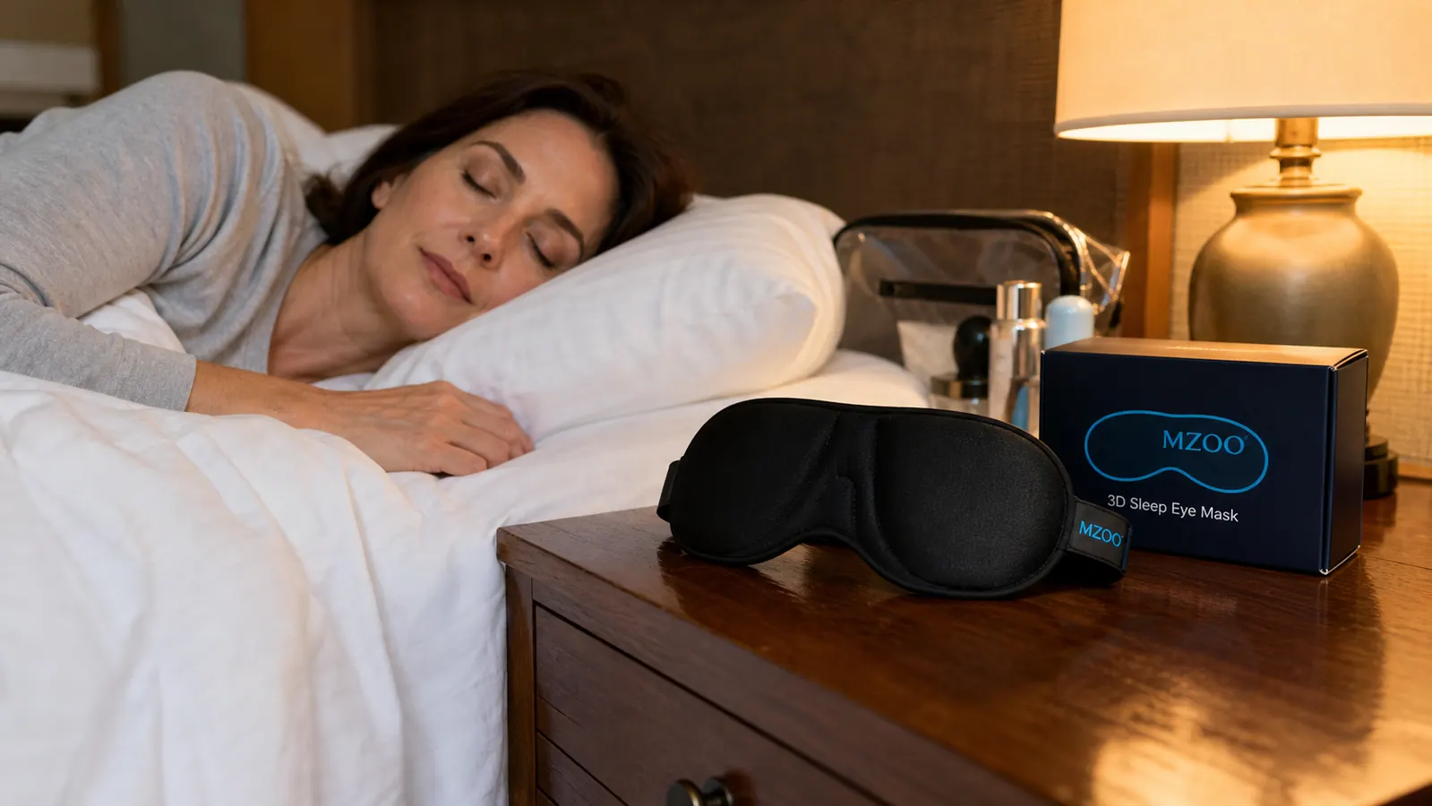 Close-up of the MZOO 3D sleep eye mask resting on a hotel nightstand next to a dim lamp and travel items